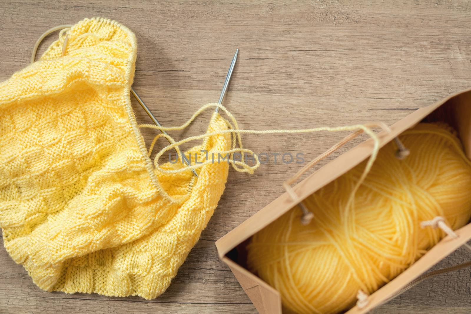 Light yellow knitting wool and knitting needles on wooden background. Top view.copy space. Knitted fabric and yarn on a wooden surface.