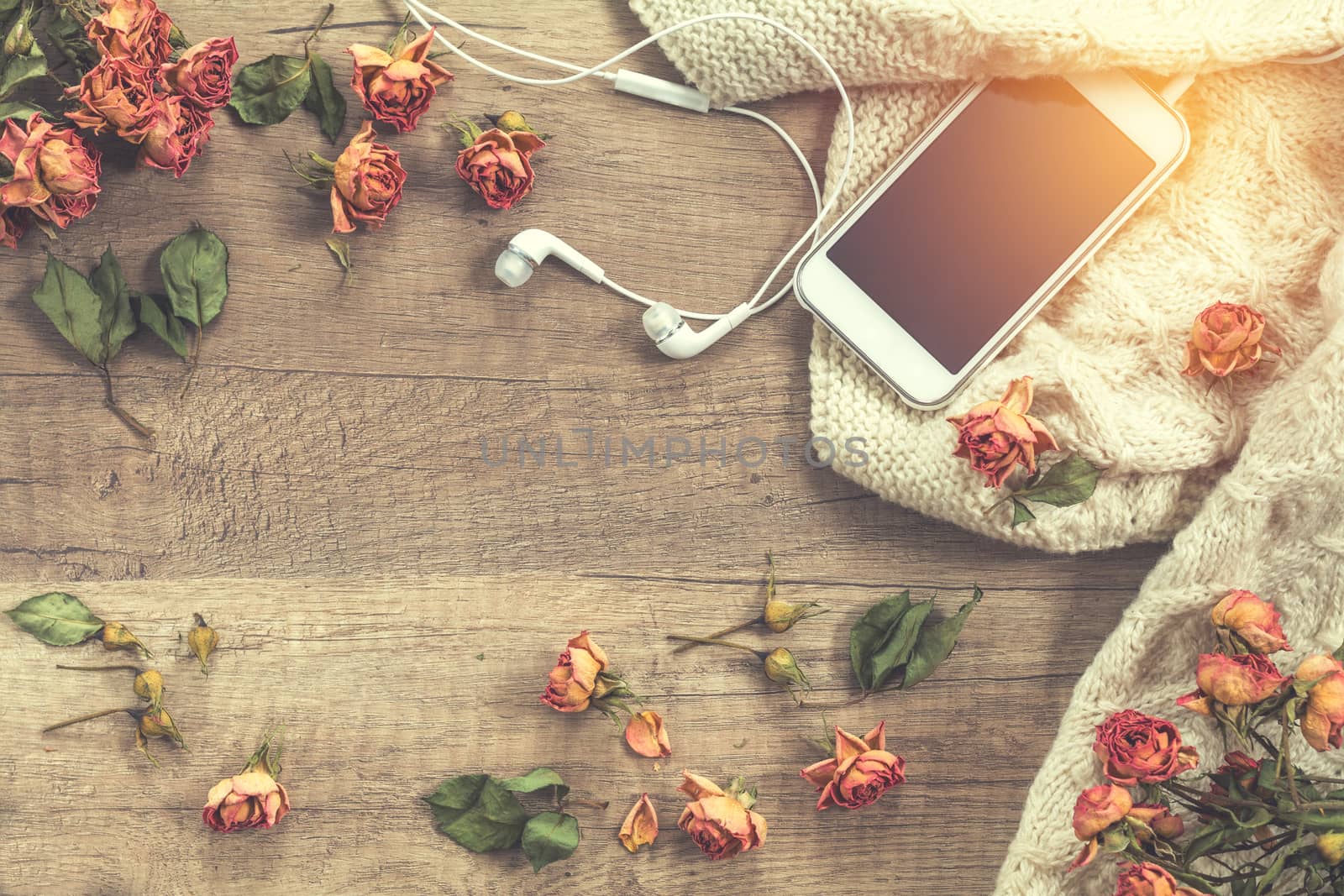 White knitting wool, dried roses flowers, mobile phone and headphones. Beautiful romantic female’s background. Toned in instagram style.