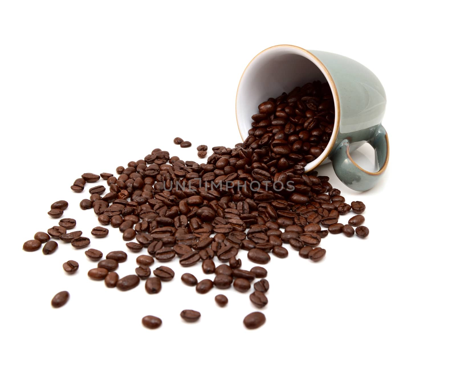 Aromatic roasted coffee beans pouring out from a green china mug on a white background