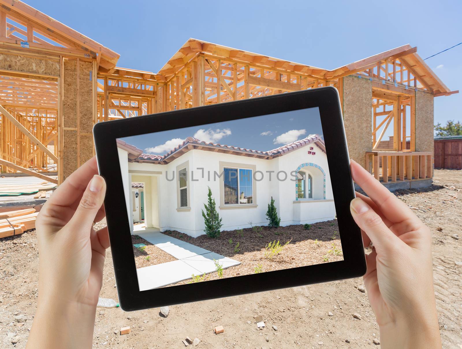 Female Hands Holding Computer Tablet with Finished House on Screen, Construction Framing Behind.