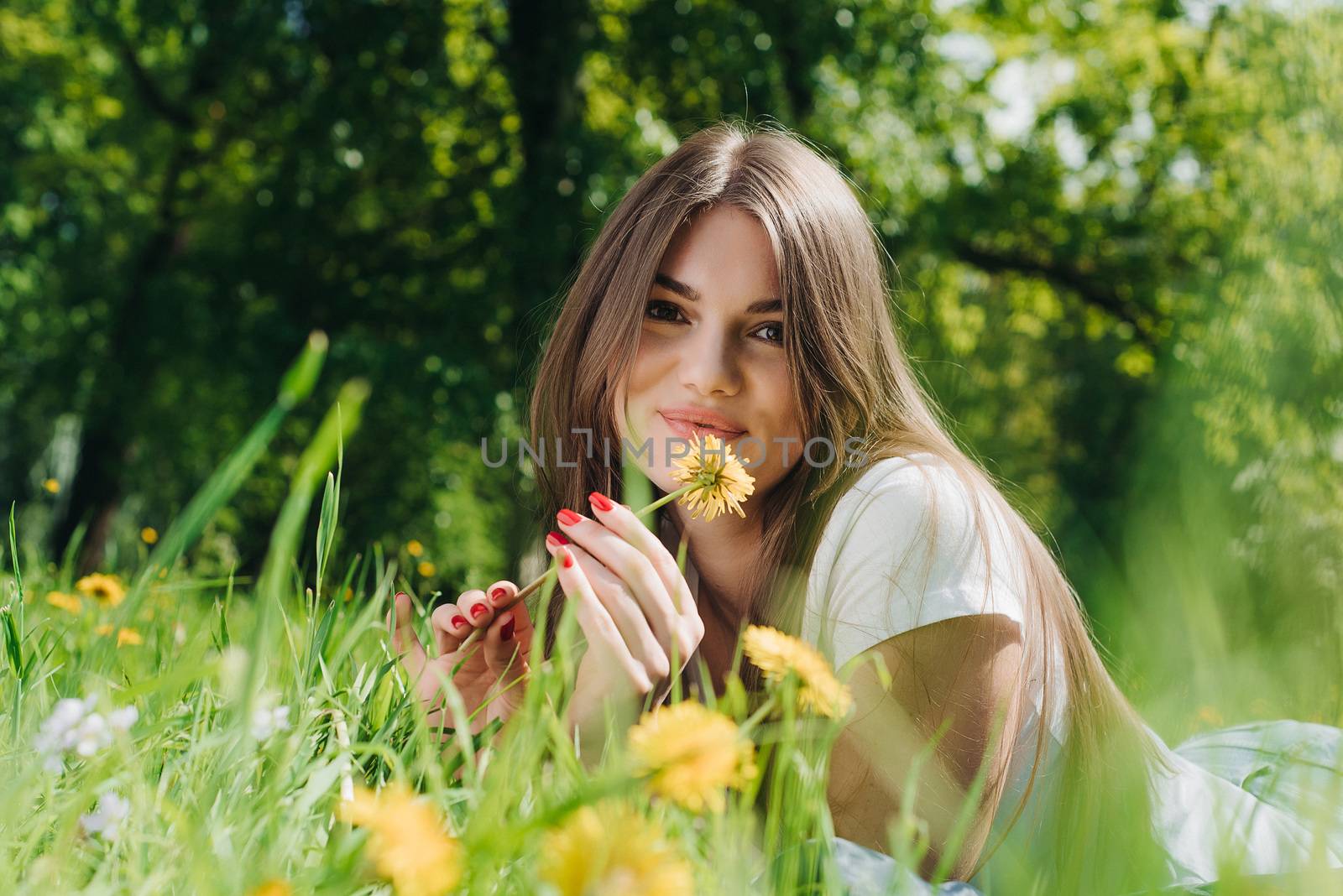 Beautiful young woman laying on grass with dandelion flowers in park