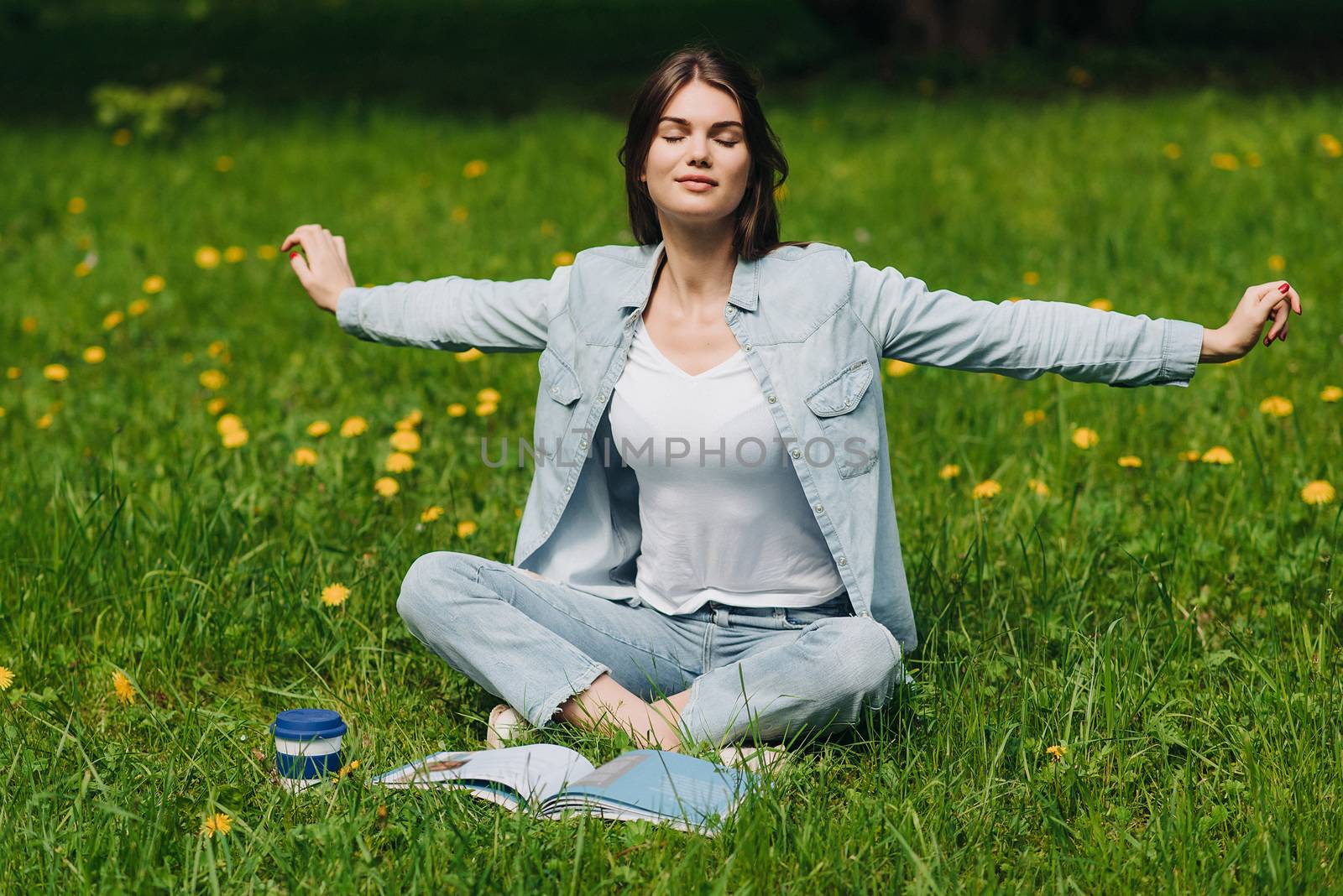 Beautiful young woman enjoy nature sitting in park with book and coffee