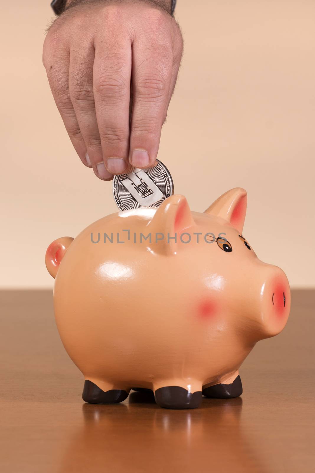 man inserts dash coin in piggy bank on top of wooden table.
