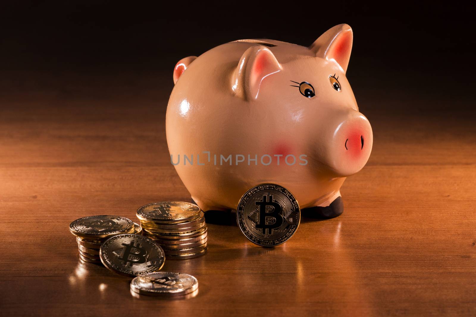 Piggy bank with bitcoins on top of wooden table.