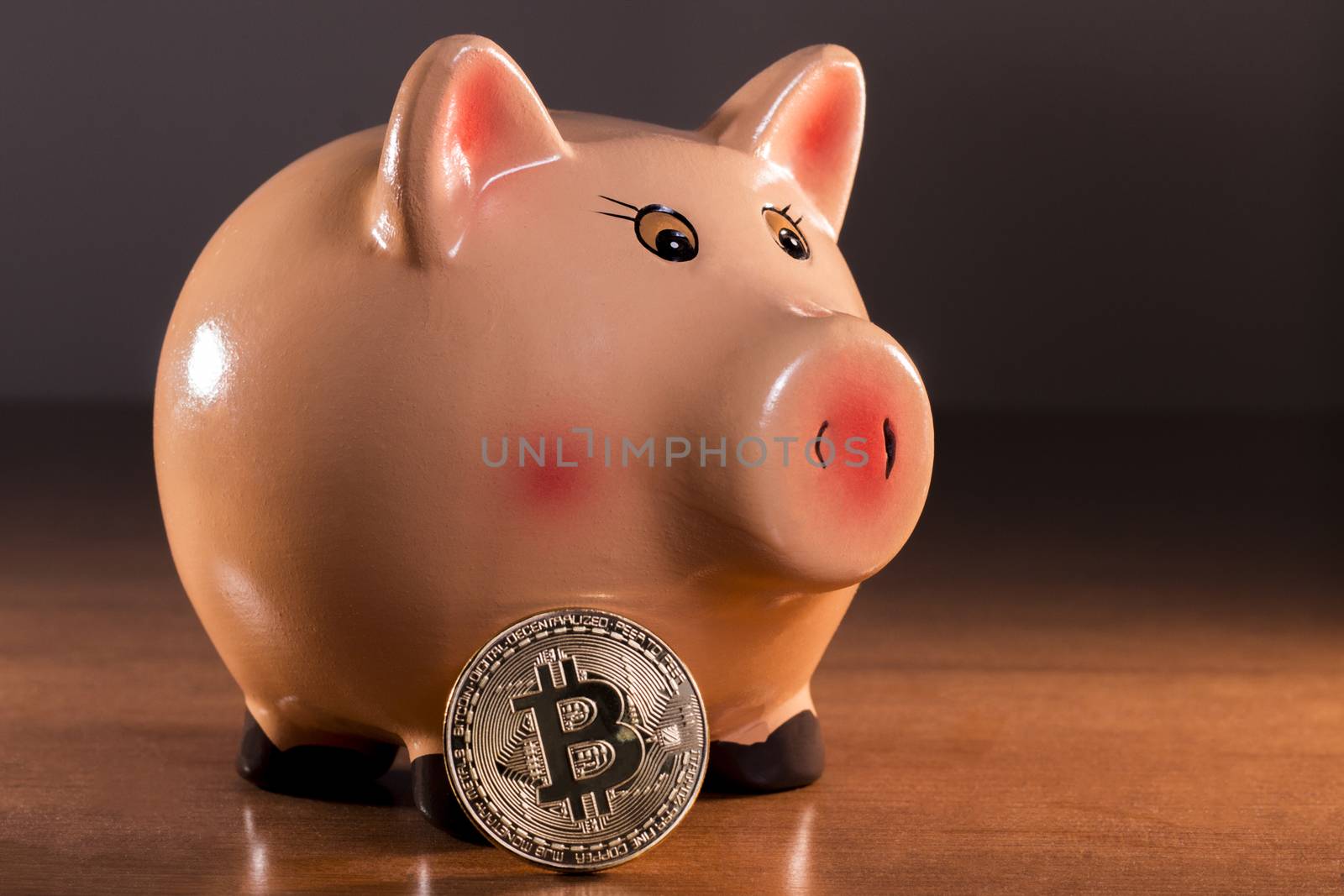 Piggy bank with bitcoin on top of wooden table.