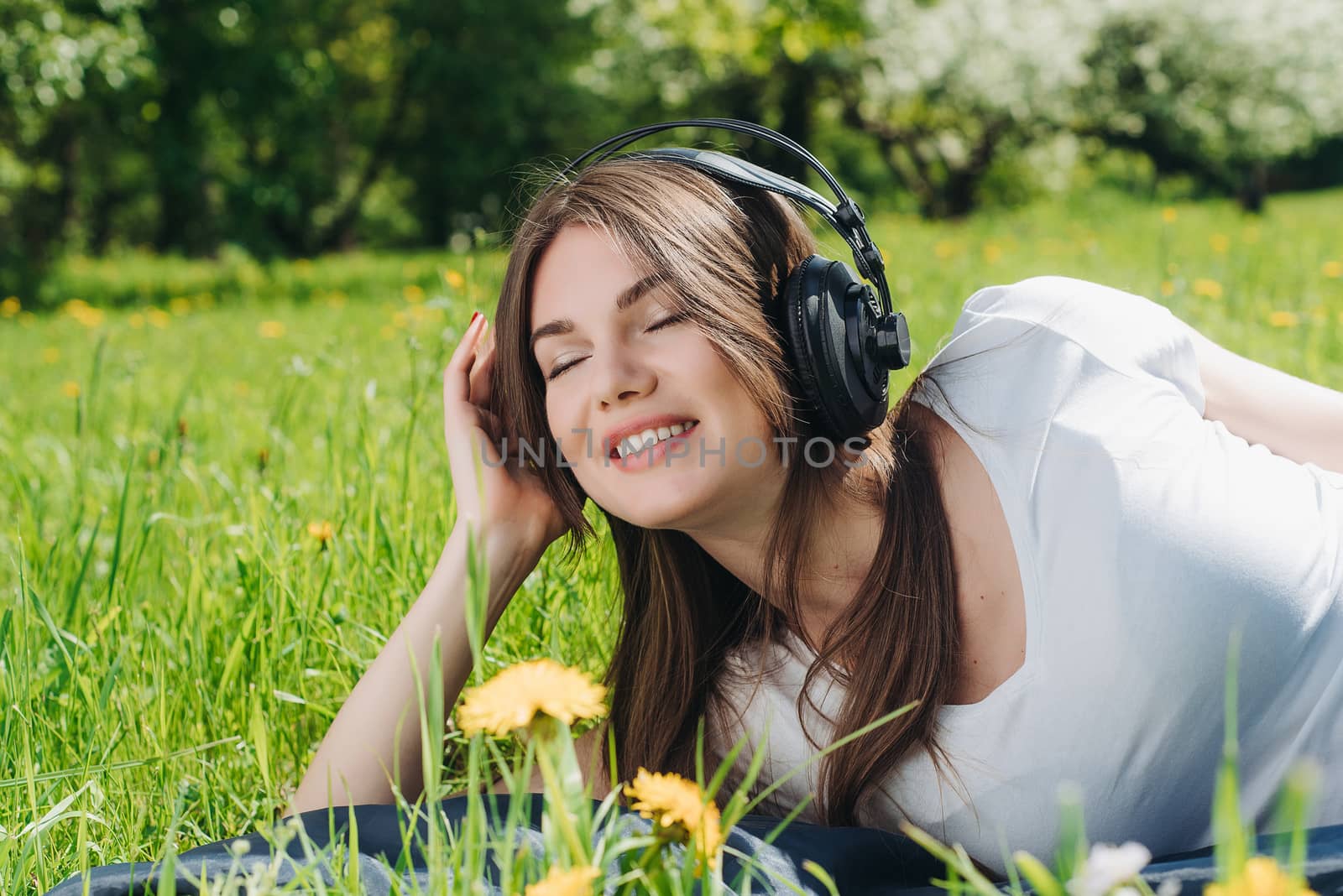Young brunette woman with headphones listening to the music outdoors on sunny summer day