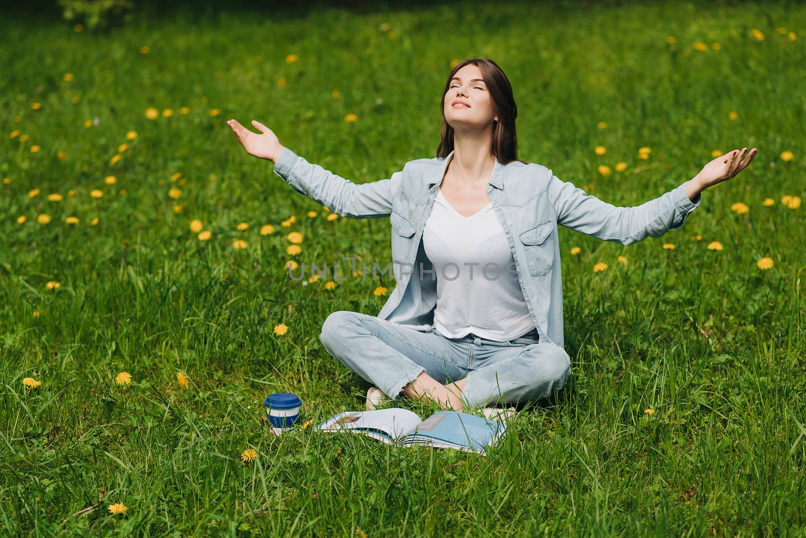 Beautiful young woman enjoy nature sitting in park with book and coffee