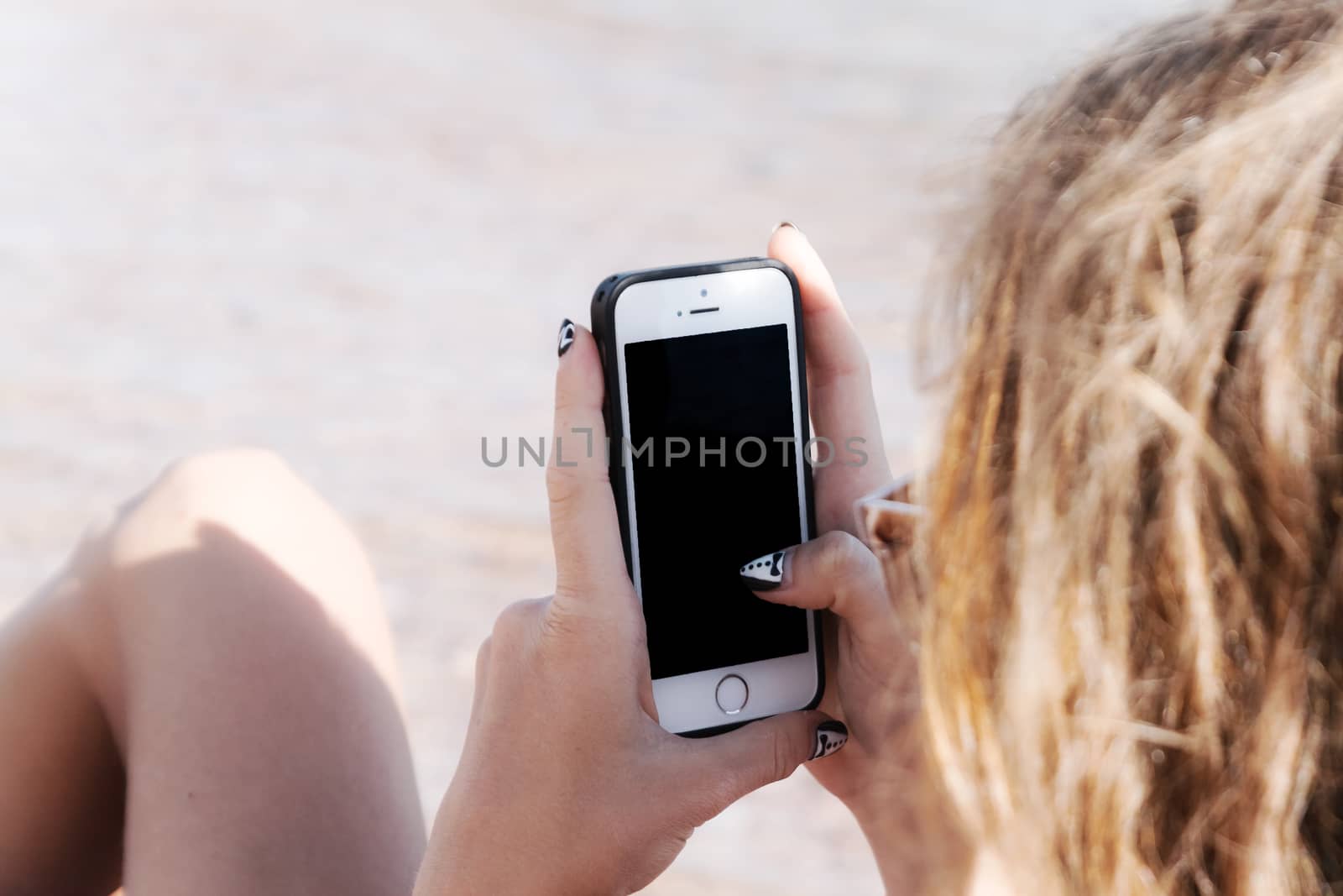 A young tanned woman looks into a smartphone through sunglasses on a lounger. The concept of a lifestyle is always on the Internet.