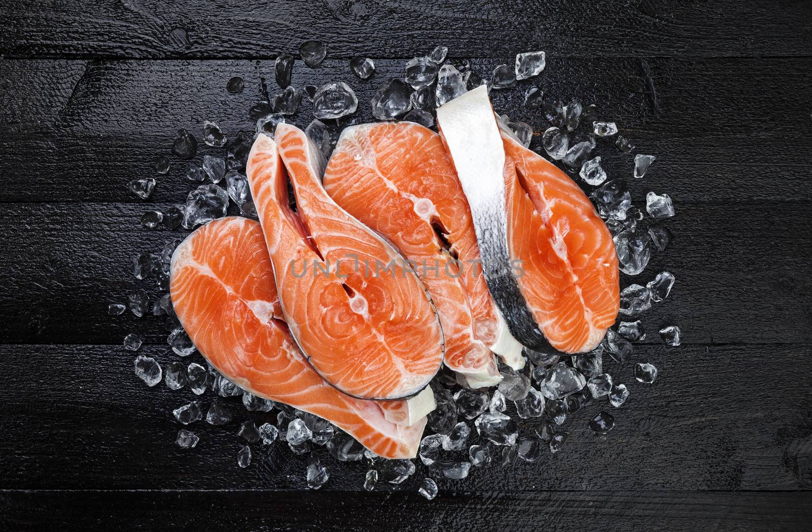 Salmon steaks on ice on black wooden table top view