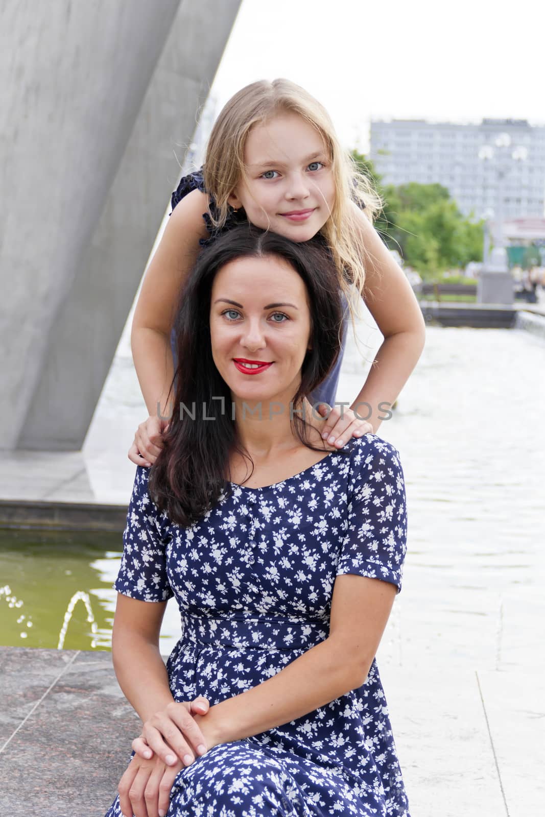 Embracing mother and daughter near fountain in summer time
