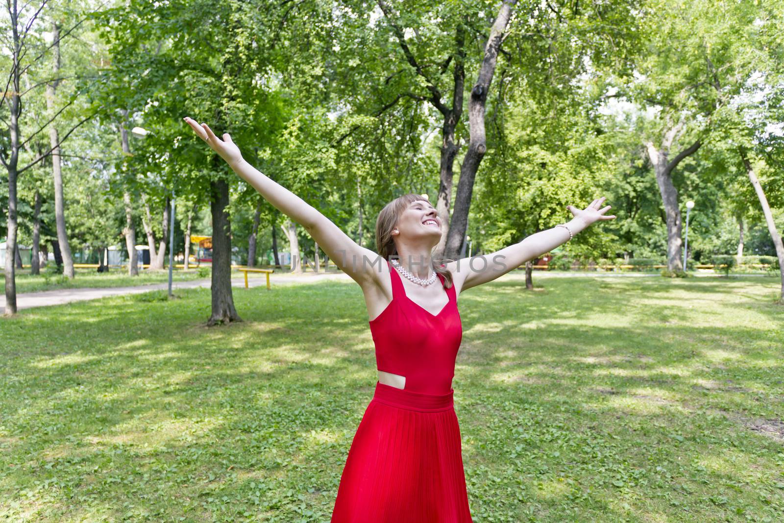 Lady in red are standing with upwards hands at summer day