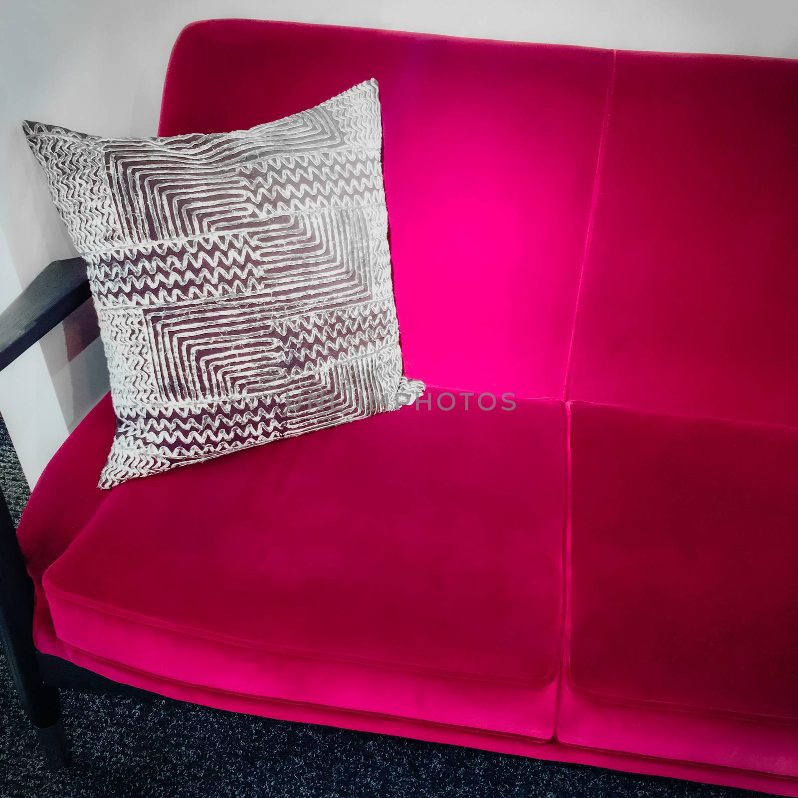 Vibrant pink velvet sofa with ornamental cushion. Luxurious furniture.