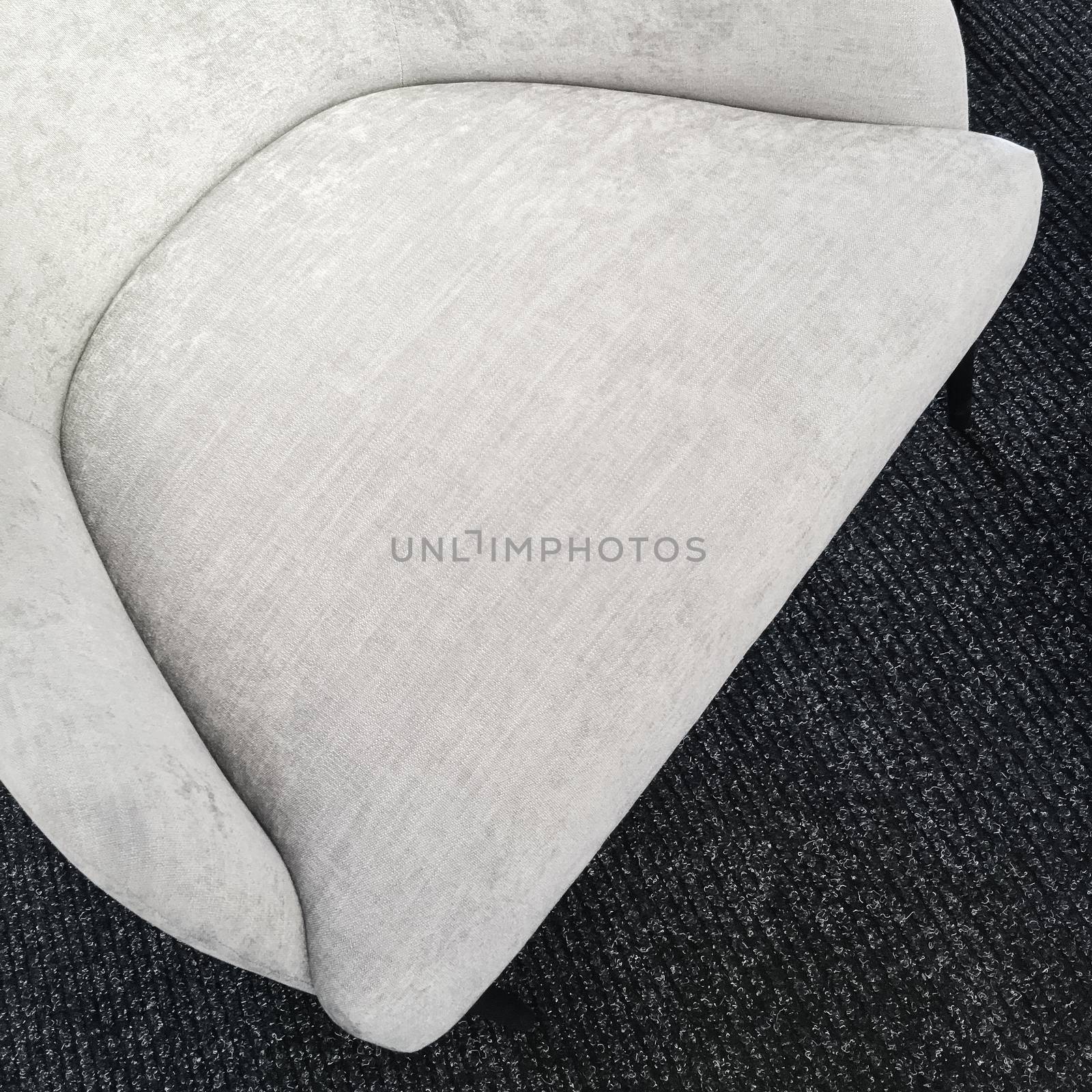 Empty seat of a simple gray armchair on dark carpet floor.