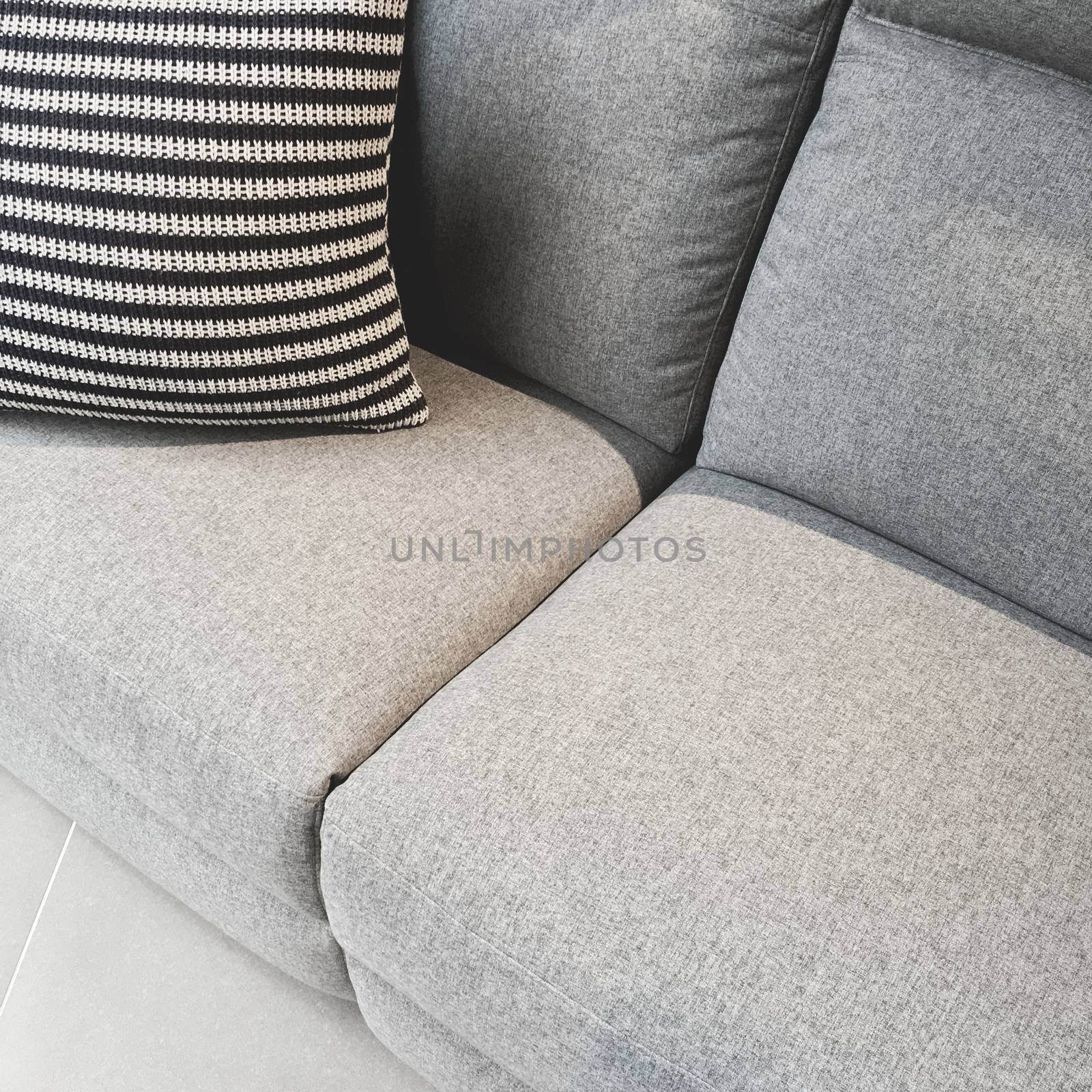 Striped cushion decorating a gray textile sofa by anikasalsera