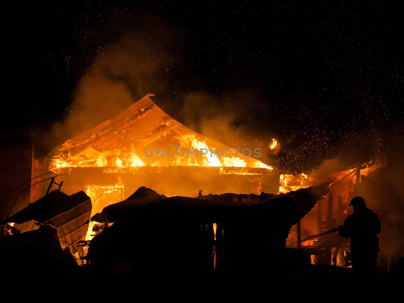 Arson or nature disaster - firefighter at burning fire flame on wooden house roof