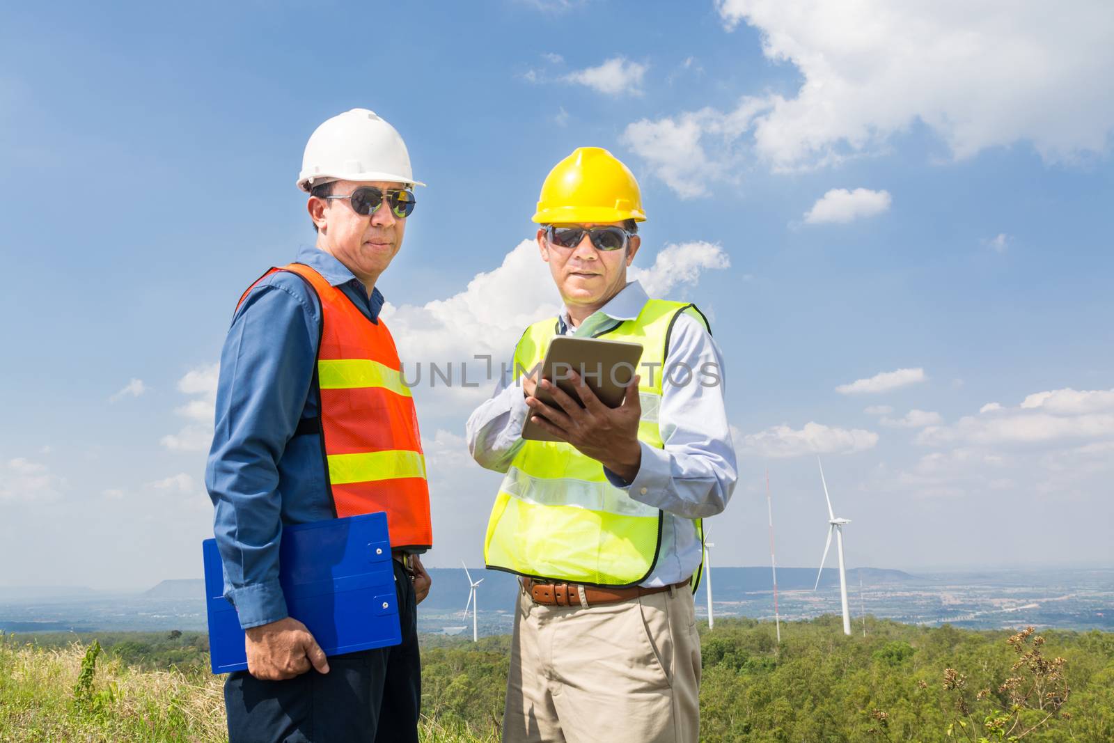 Alternative Power or Renewable Energy Technology Project Development Concept, Engineer and Architect discuss over Digital Wireless Tablet and Clipboard while working at Wind Turbine Power Generator Tower site.