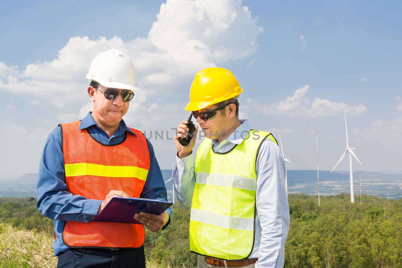 Male Engineer and Architect working Together with Hand-Held Transceiver Radio and Clipboard at Wind Turbine Power Generator Field as infrastructure construction Project Development Teamwork