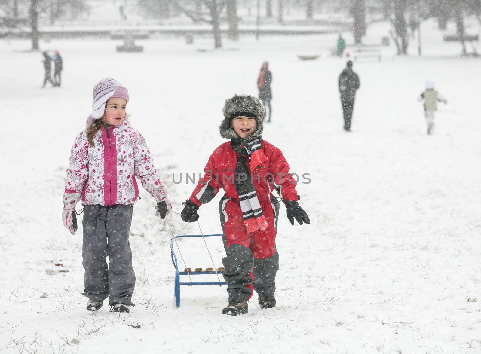 Two happy kids are pulling a sled in the snow during a cold winter day.