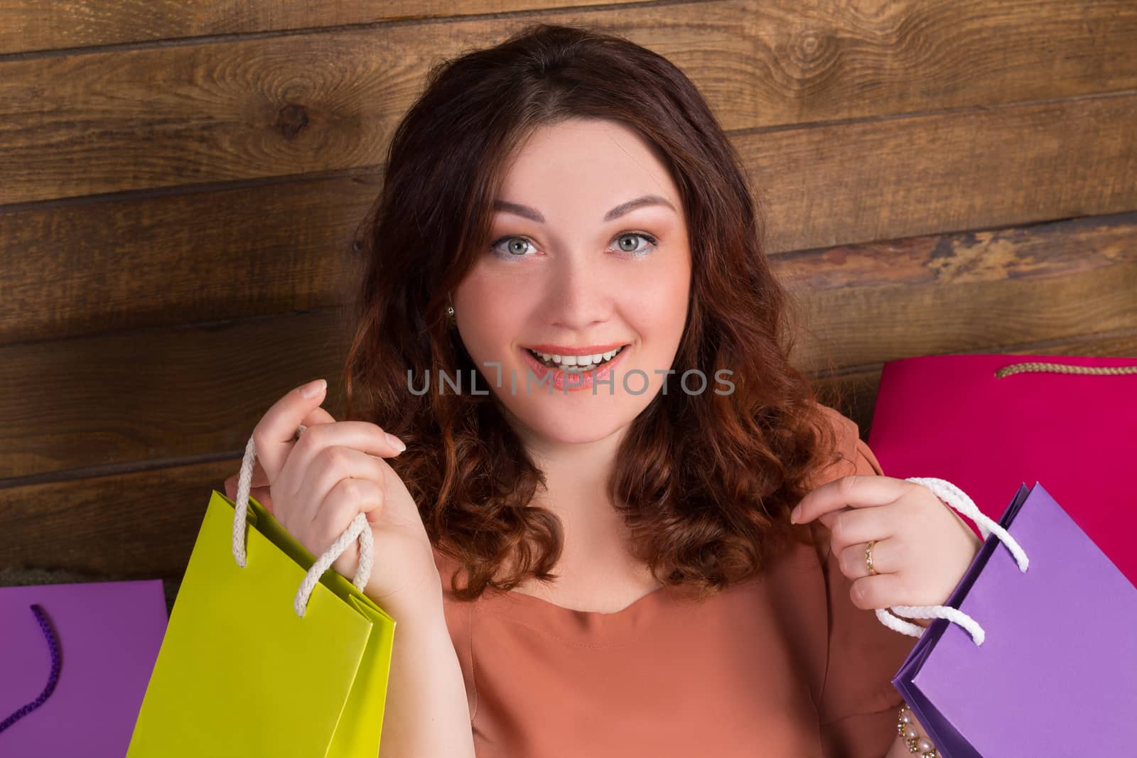 Woman after shopping with colourful paper bags with wooden wall on background