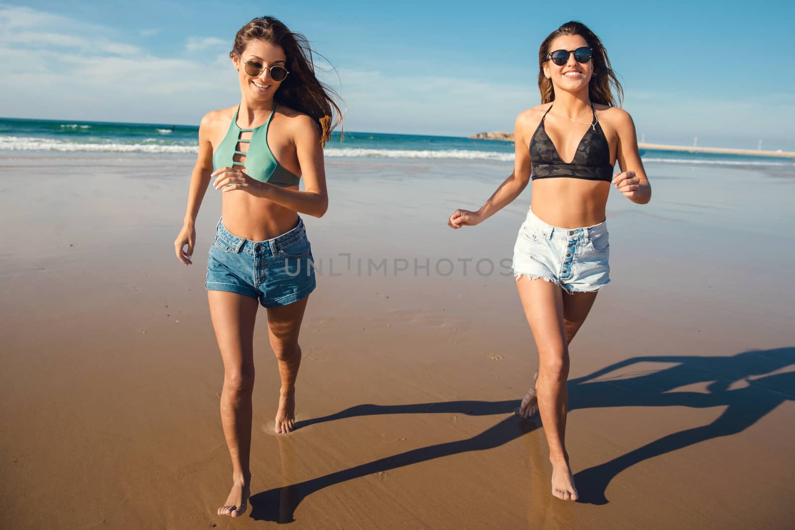 Two beautiful female friends in bikini running at the beach and having fun together