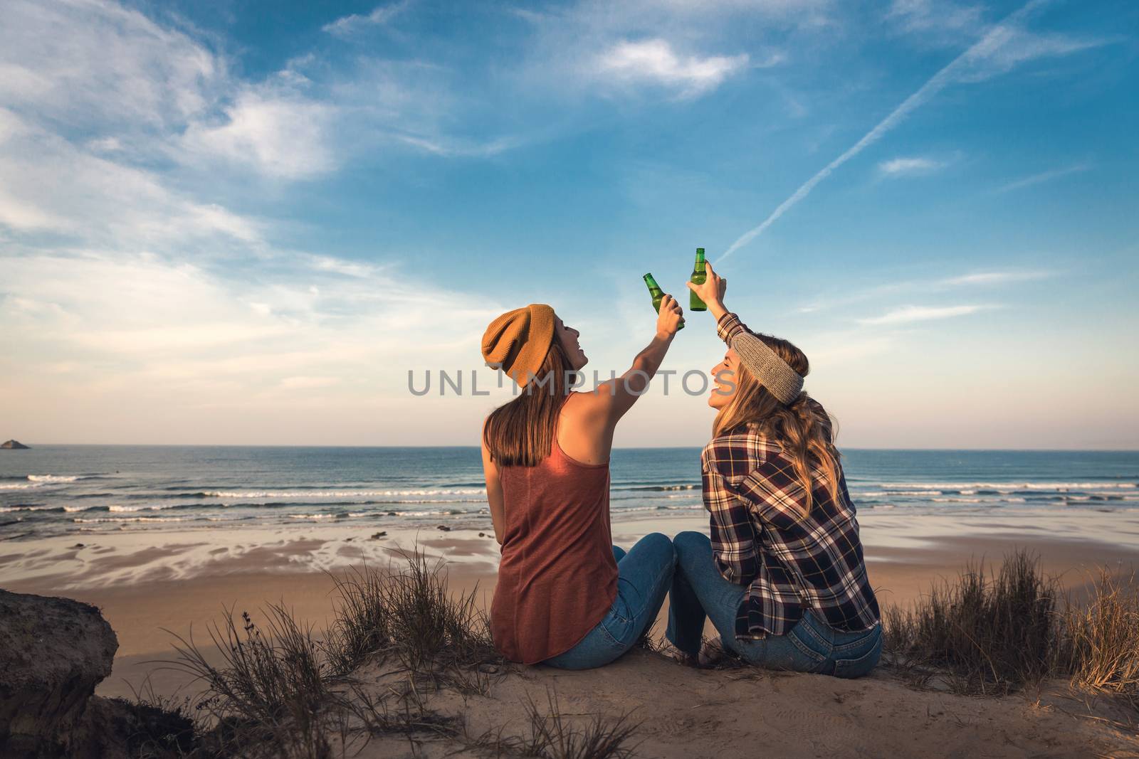 Two best friends sitting on the coastline toasting to friendship