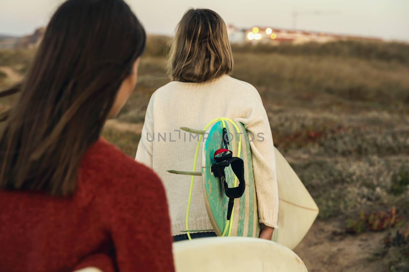 Two female surfers walking near the coastline with surfboards