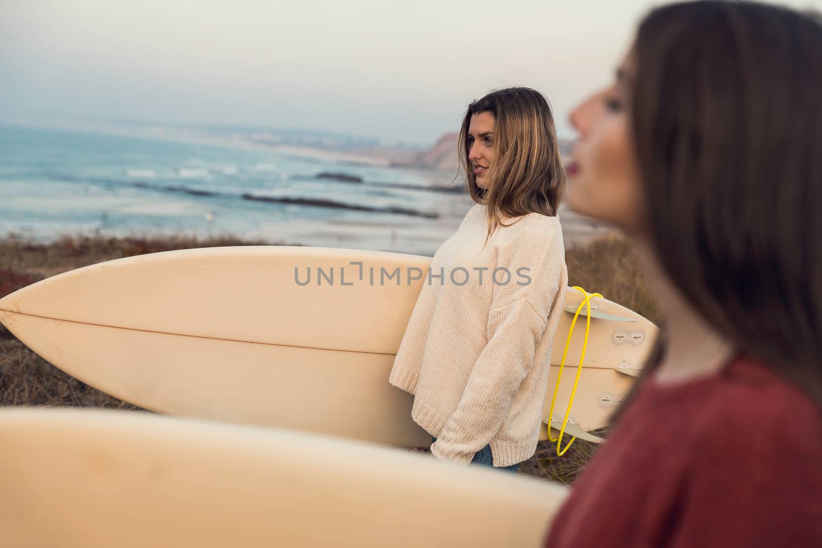 Shot of two female friends holding their surfboards while looking to the ocean