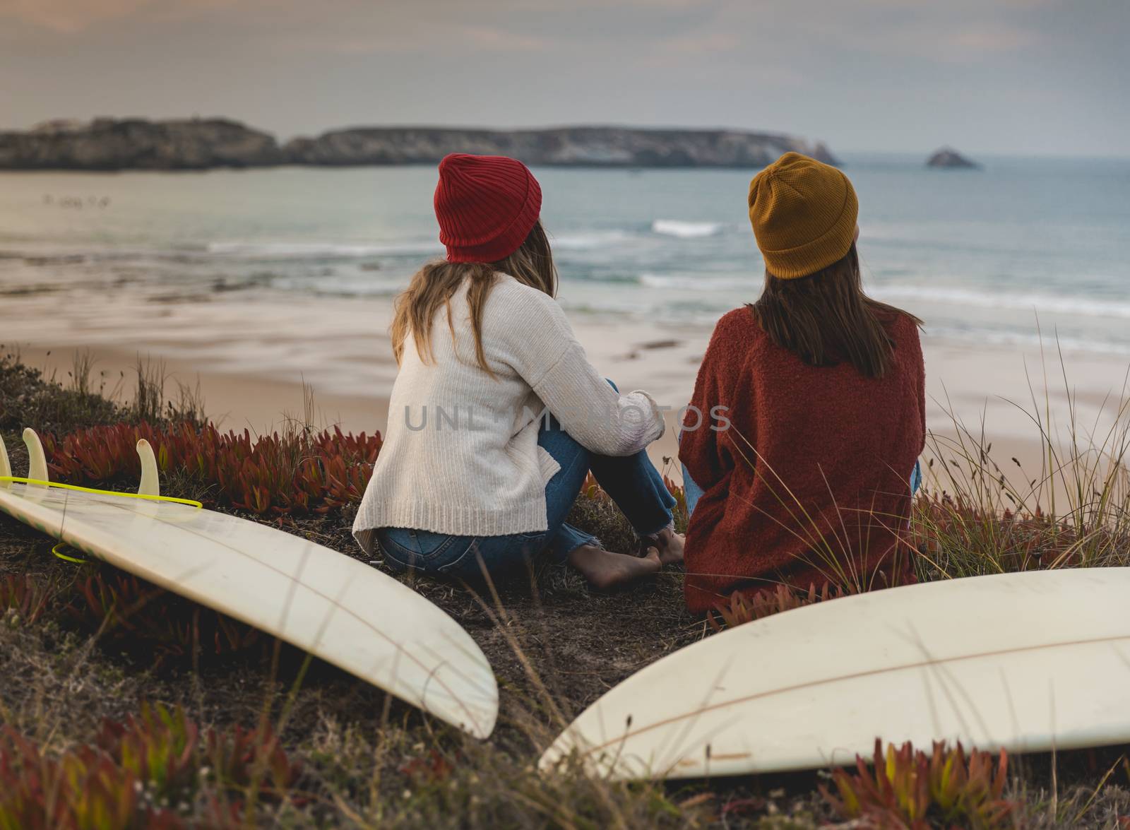 Two best friends sitting near the coastline with her surfboards while looking to the ocean