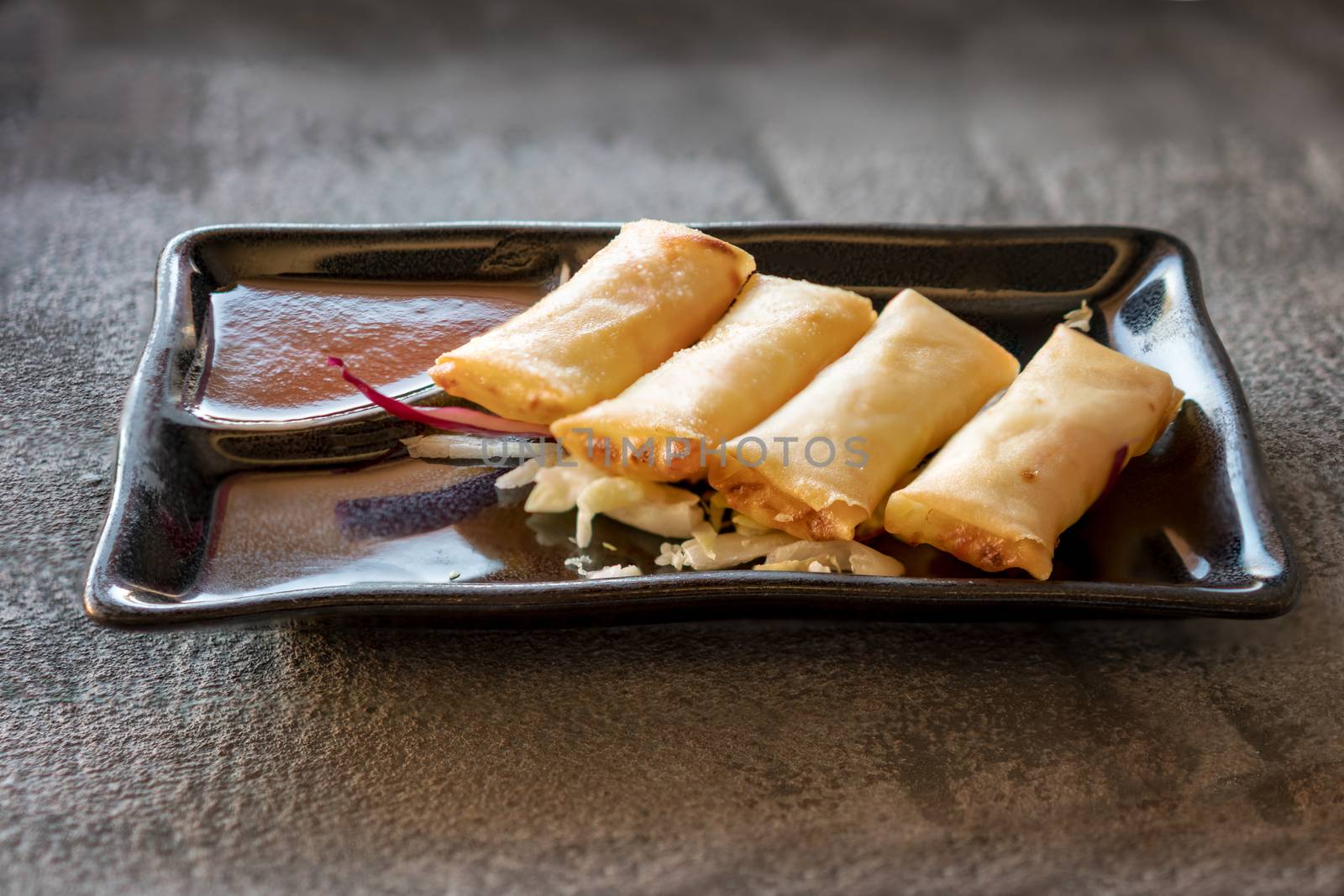 Fried spring rolls on black iron plate on grey stone slate background. side view,close up.