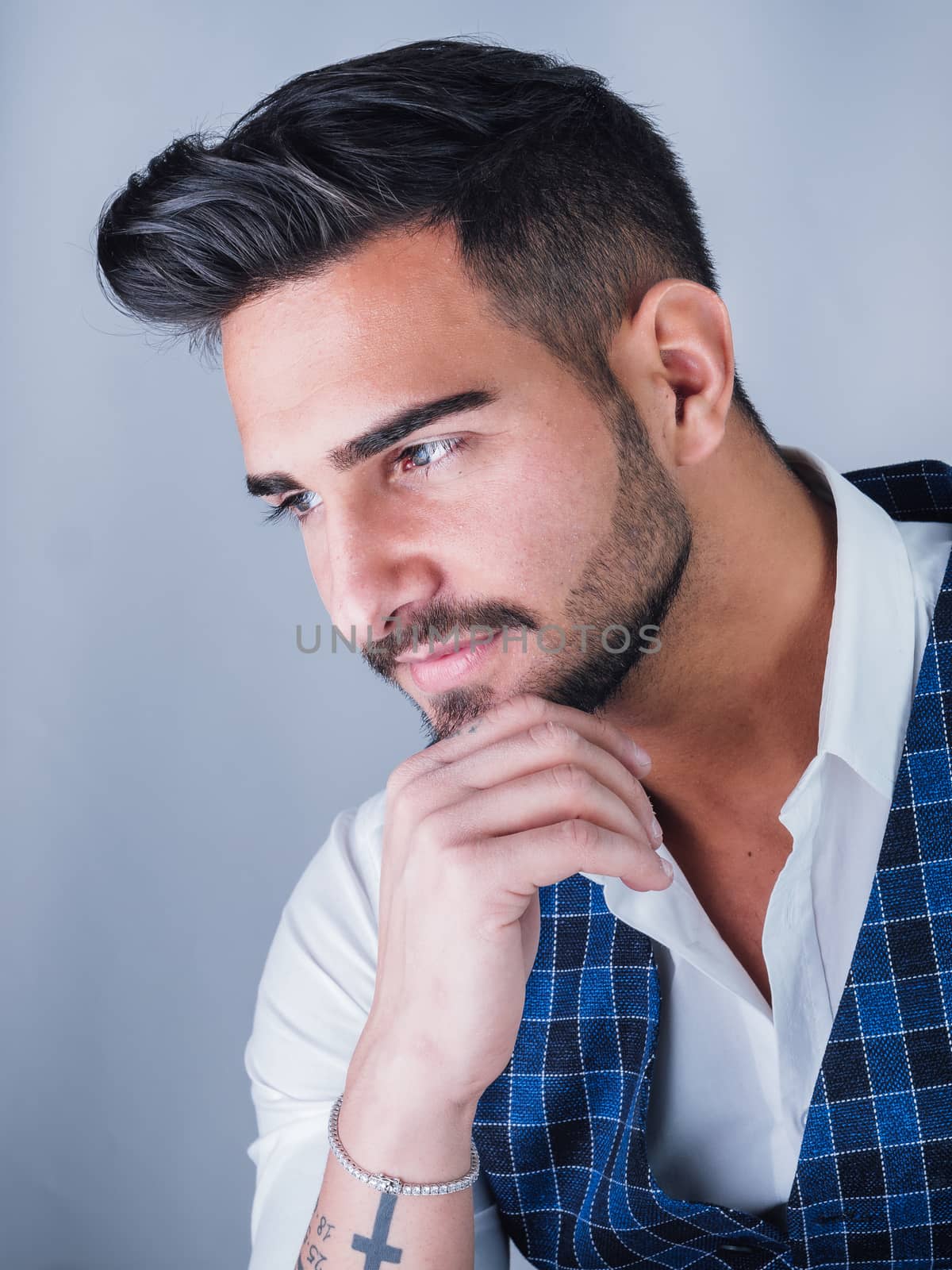 Trendy young man in studio shot wearing elegant vest and white shirt, looking away to a side