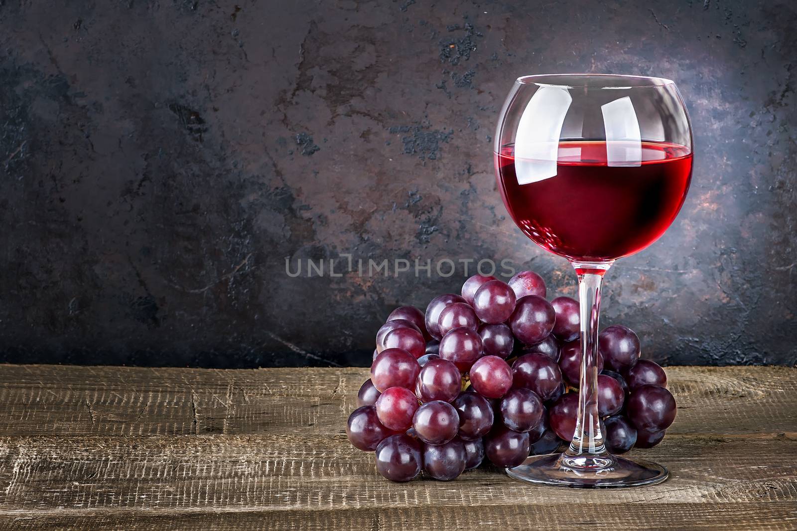 Wineglass with red wine and red grapes on wooden table. Dark background.