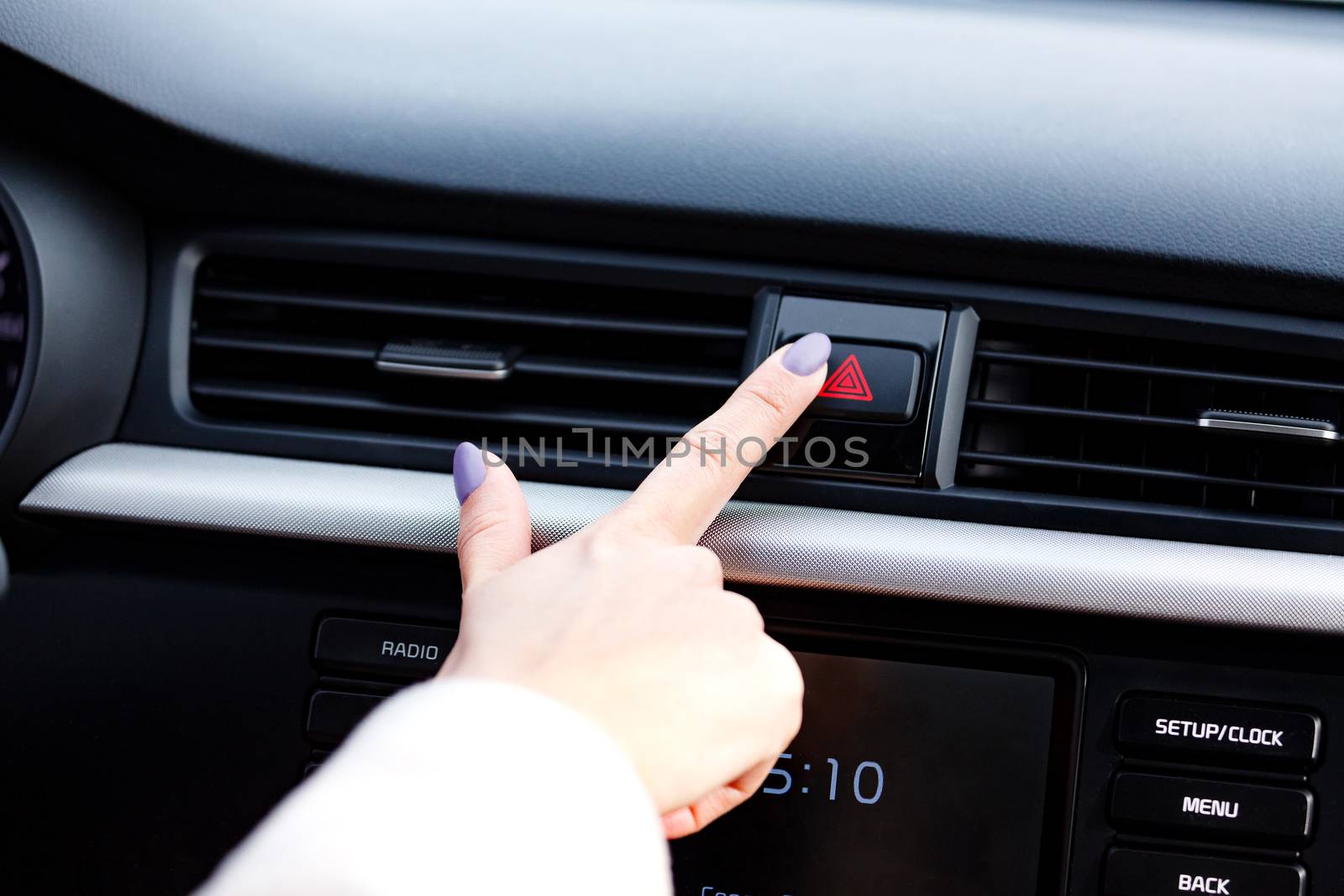 Closeup shot of woman's manicured finger pressing the emergency button on a car's dashboard