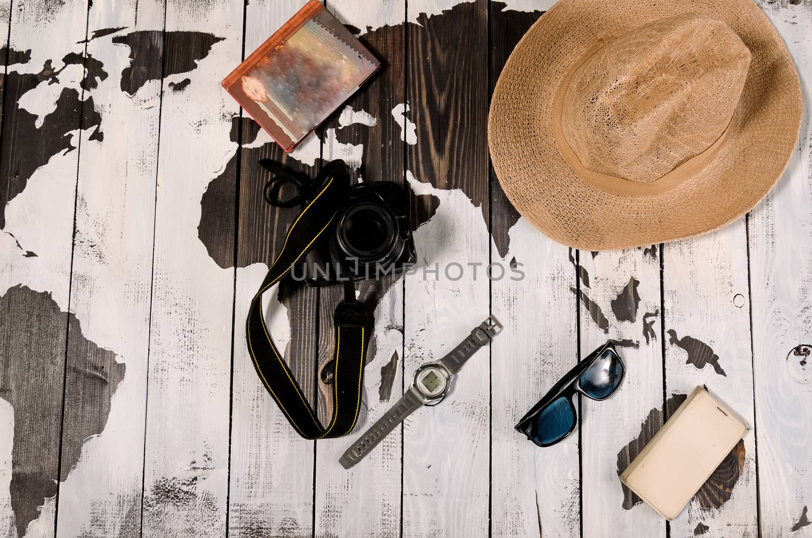 Table with open map showing plans for travelling and related items including watch smartphone sunglasses hat notebook and camera on wooden background with copyspace left
