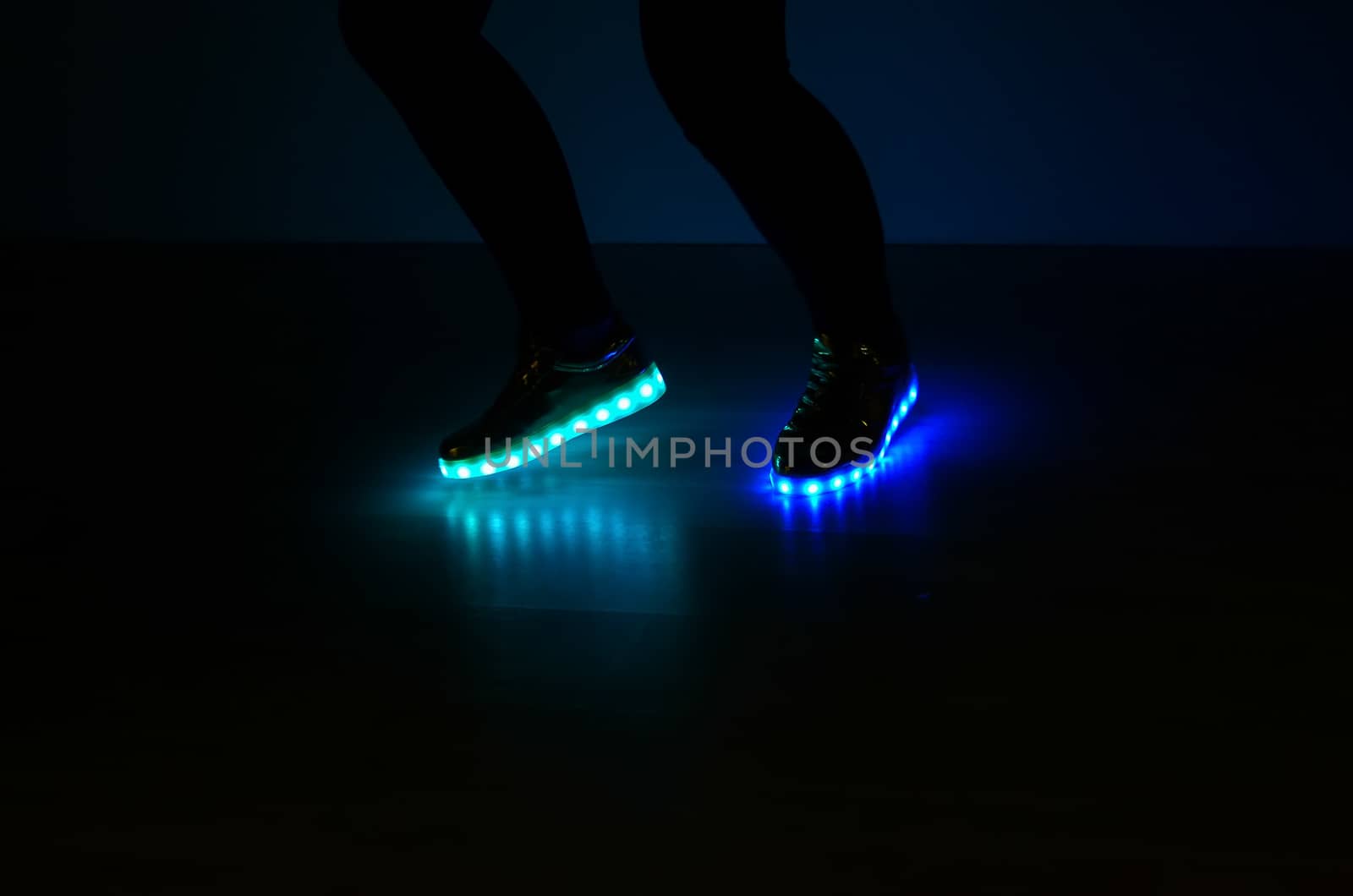 Fashionable sneakers with neon LED lighting on the legs of a girl with blue and azure colors in the dark .Different colors of neon lights soles sneakers are present.