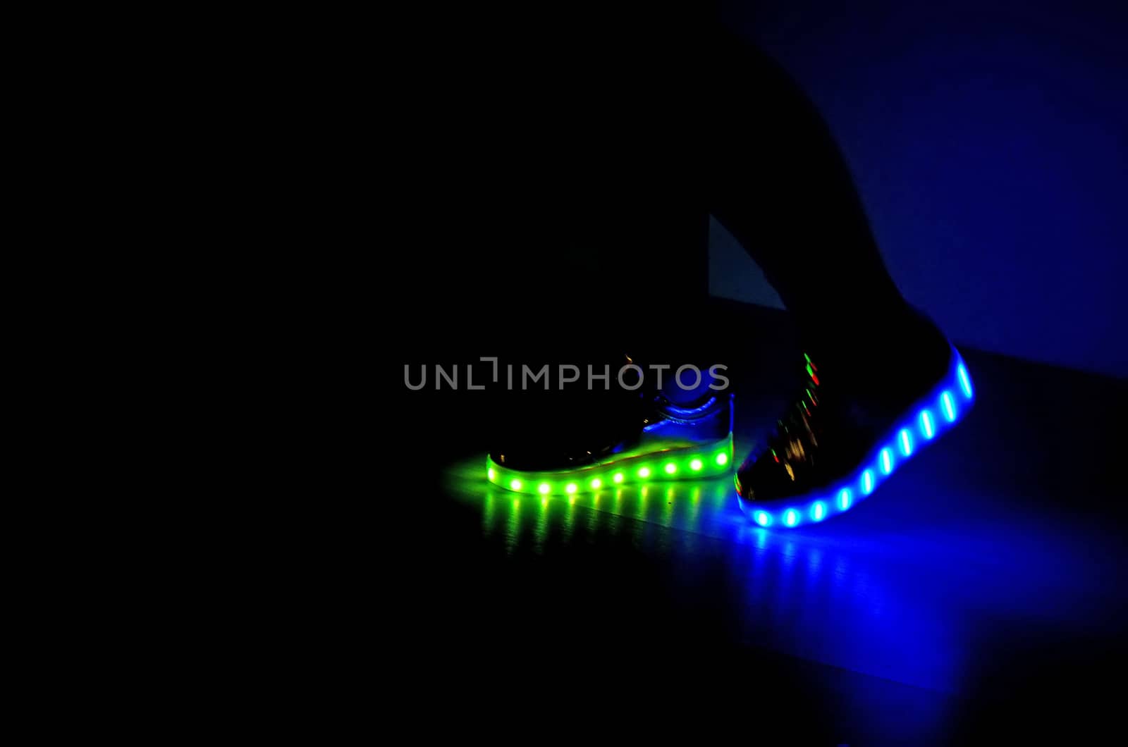 Fashionable sneakers with neon LED lighting on the legs of a girl with green and blue colors in the dark .Different colors of neon lights soles sneakers are present.