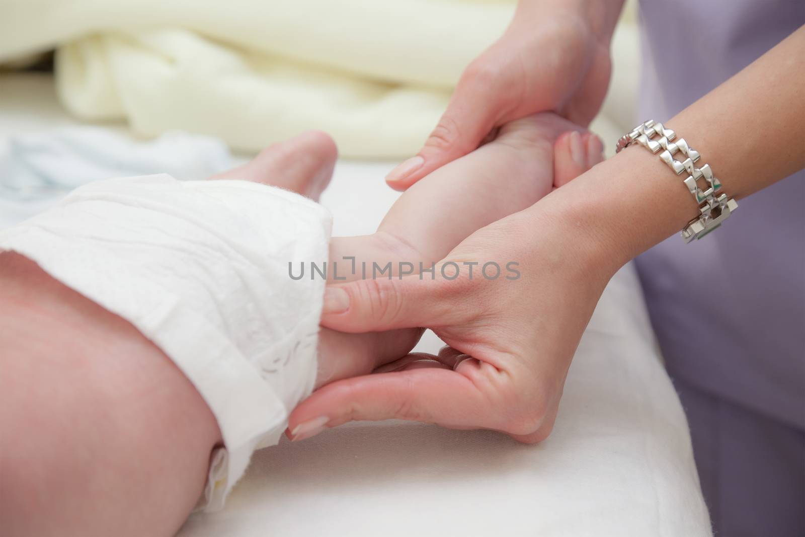 Close-up of female hands massageing jently small baby legs.