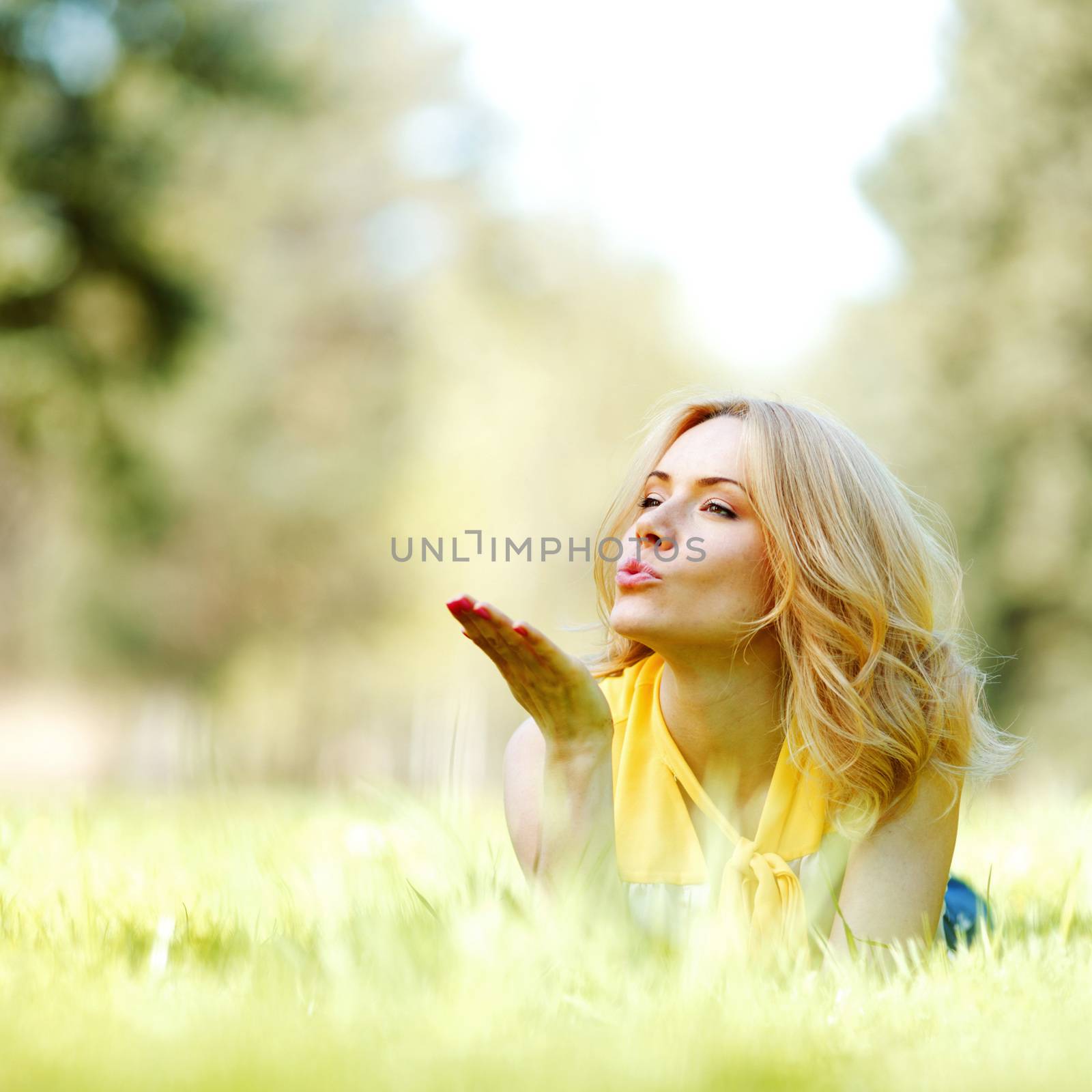 Young woman blows a kiss lying on green grass meadow