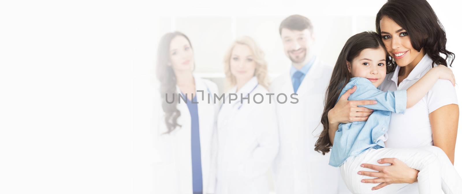 Mother holding daughter on hands, team of doctors on background, isolated on white