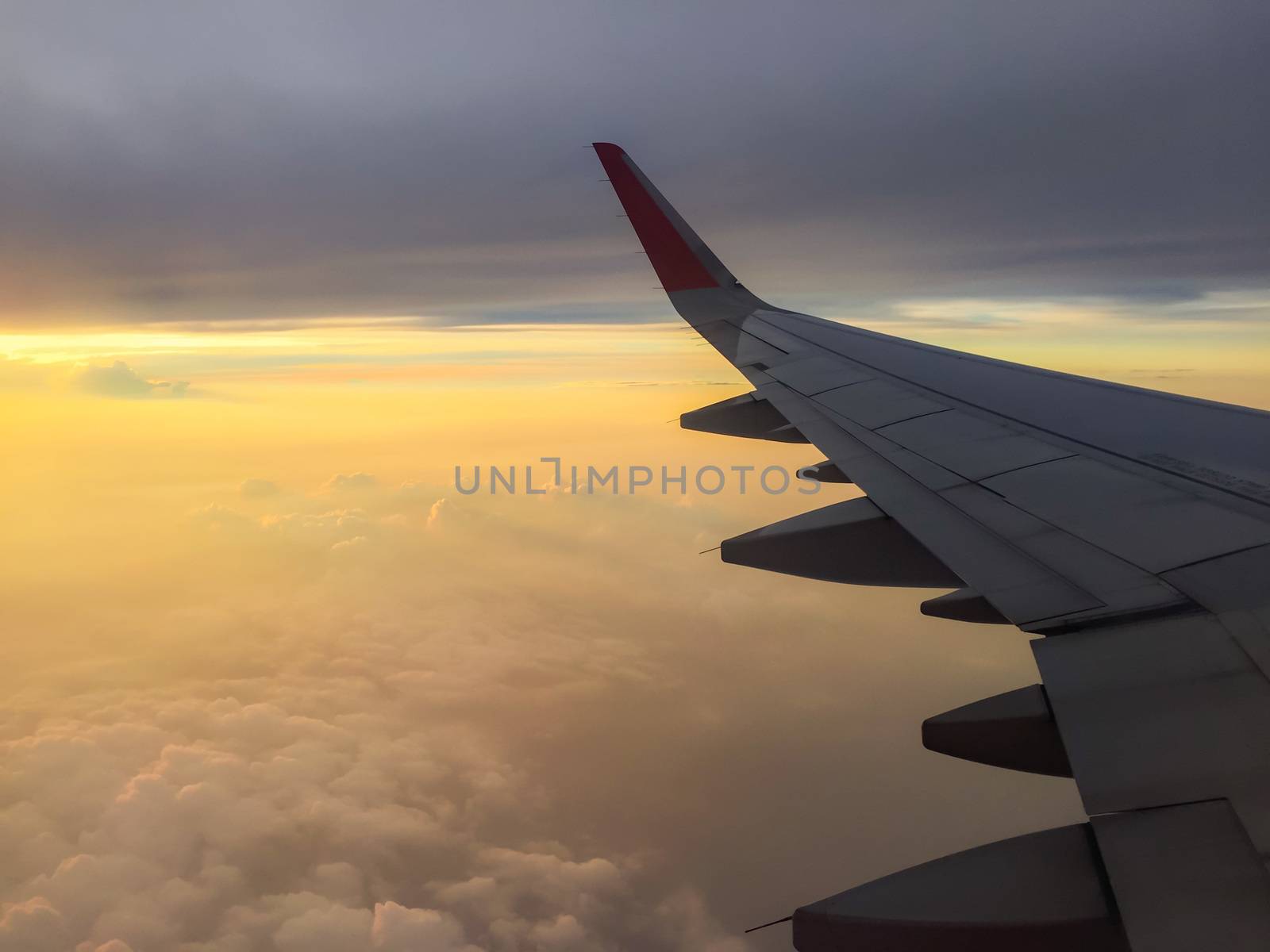 High altitude in flight passenger jet airliner airplane wing, with a cloudy sunset colourful sky.