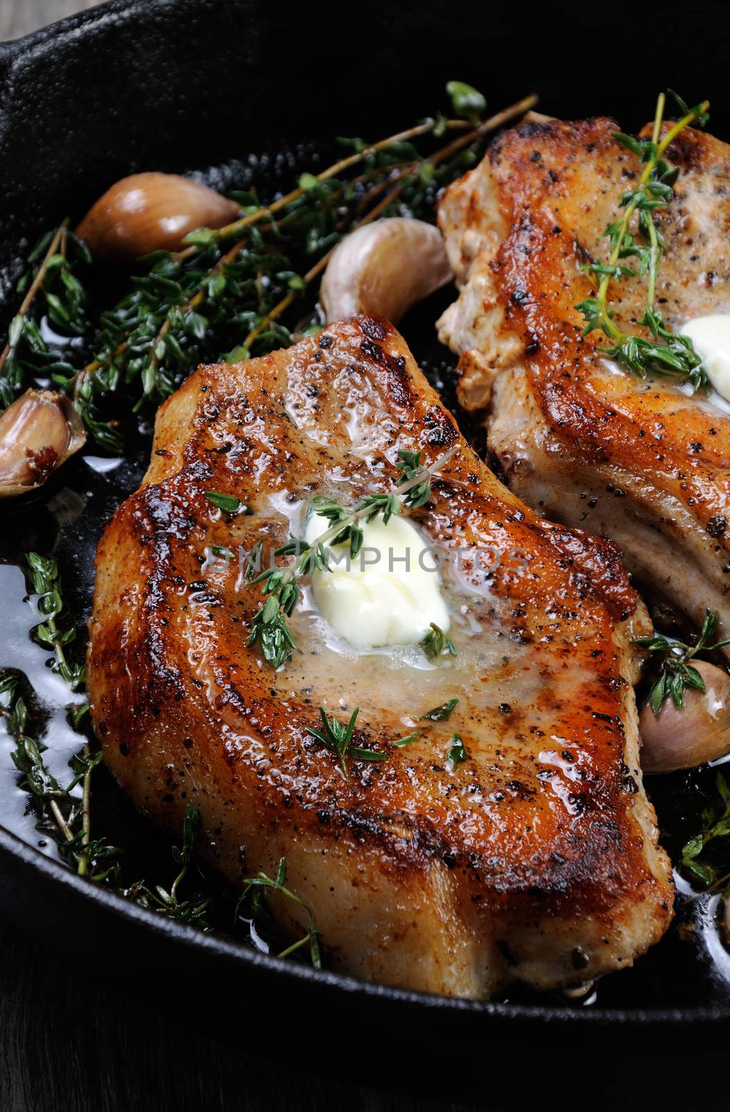 Juicy, browned pork steak on a bone in oil with garlic and herbs in a frying pan. 