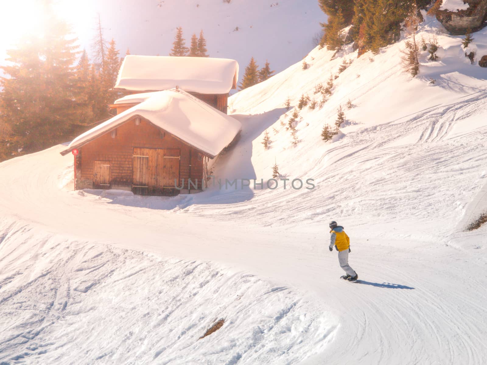 Snowboardist on a ski slope at alpine hut on sunny day, Alps.