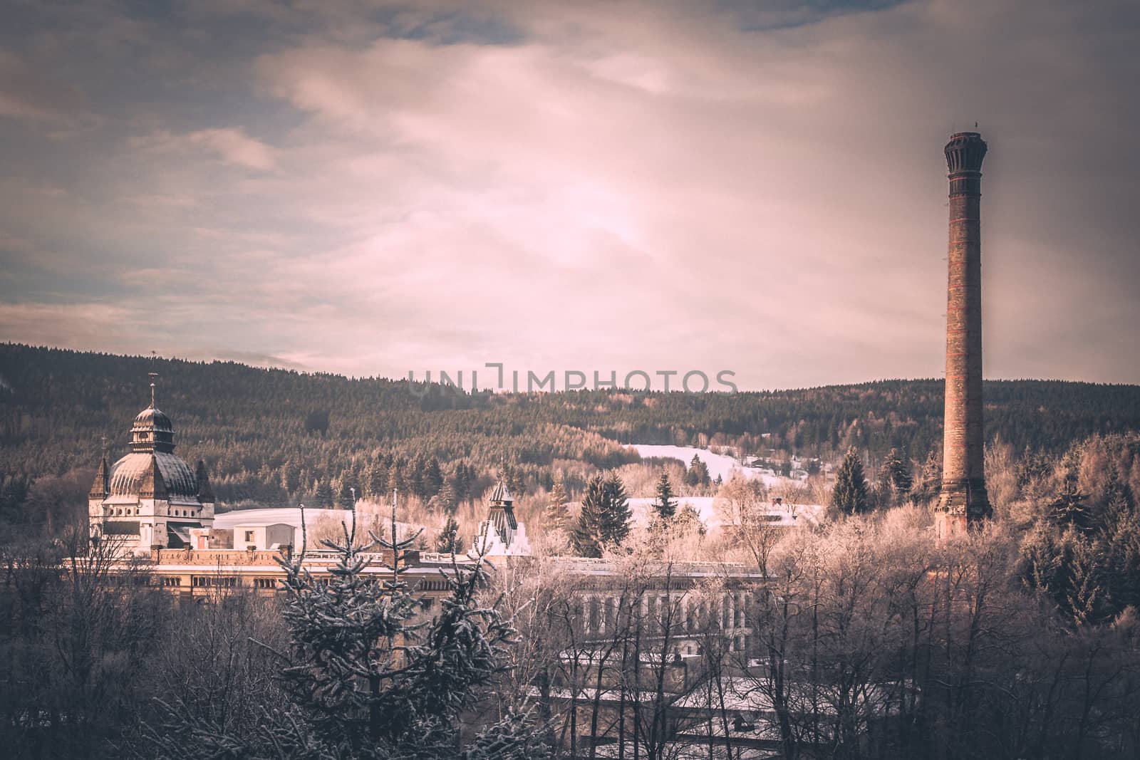 Old mountain factory with ornamental dome and high chimney in winter landscape. Vintage style image.