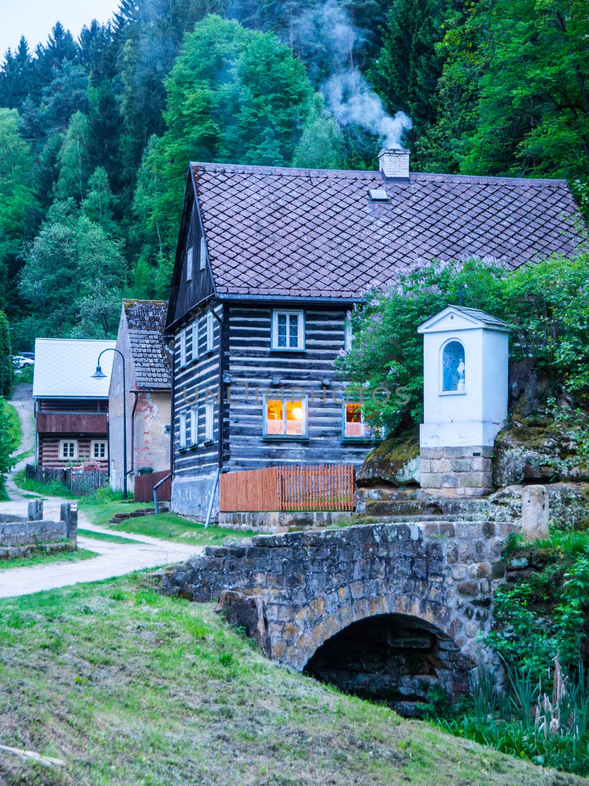 Old traditional timbered cottage with romantic with stone bridge at evening time. Czech rural architecture by pyty