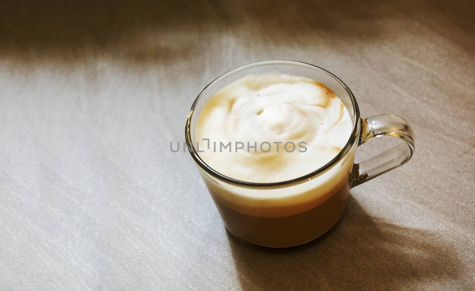 Glass mug with foamy cappuccino on a rough marbled floor . Interior shot