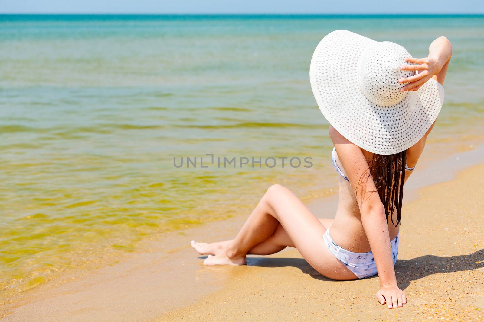 Woman in big straw sunhat sunbathing on a sandy beach. Summer holidays concept