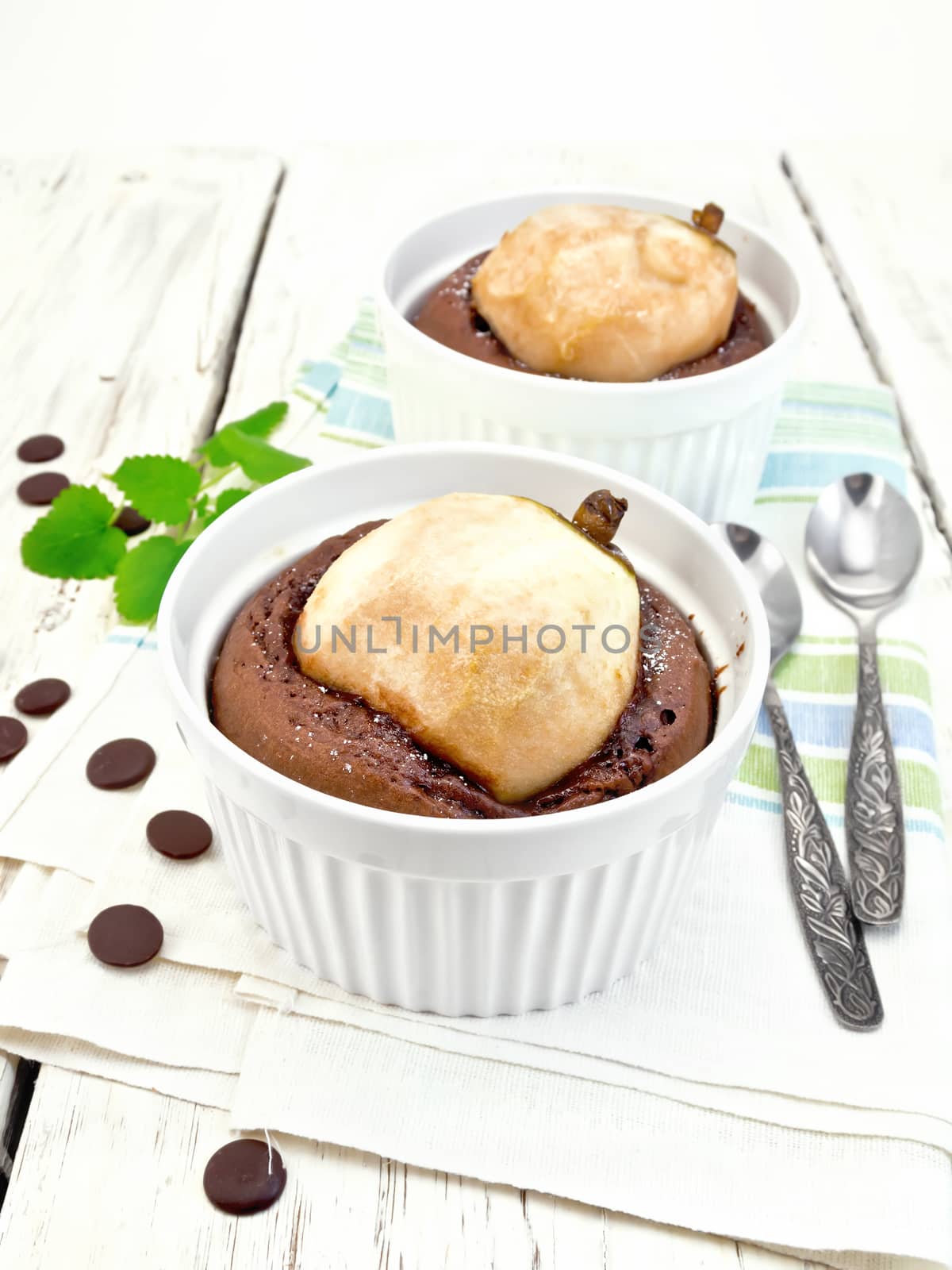 Two white bowl dessert with chocolate and pear, spoon, mint on a napkin against the background of wooden boards