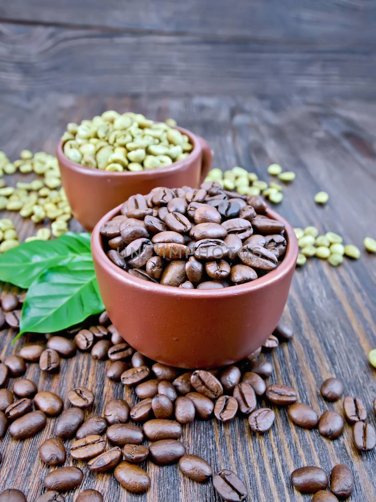 Grains of green and black coffee in brown clay cups and on a table with leaves on a wooden plank background