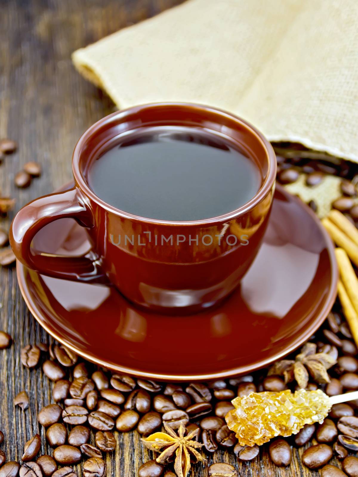 Coffee in cup brown with sugar, a bag of coffee beans, cinnamon sticks and star anise on a background of dark wood planks