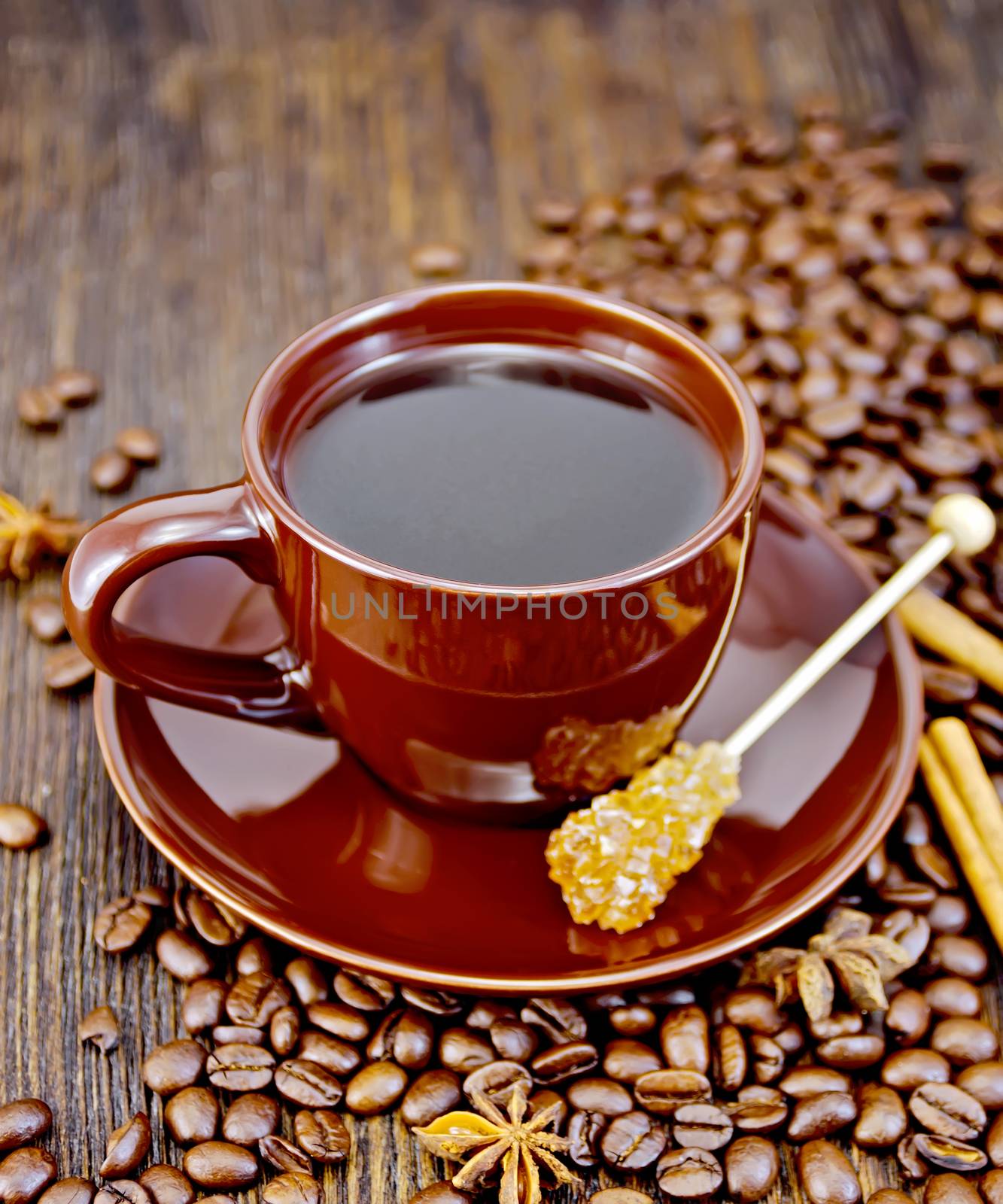 Coffee in cup brown with sugar, coffee beans, cinnamon sticks and star anise on a wooden boards background
