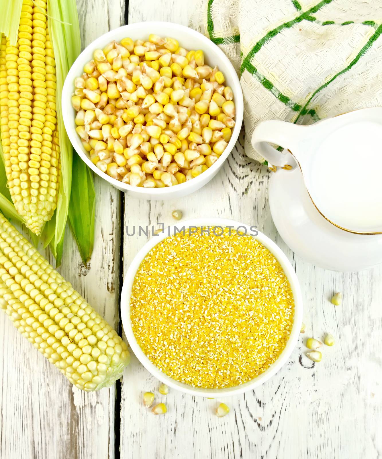 Corn grits and corn in two bowls, a napkin and cobs on the background of the wooden planks on top